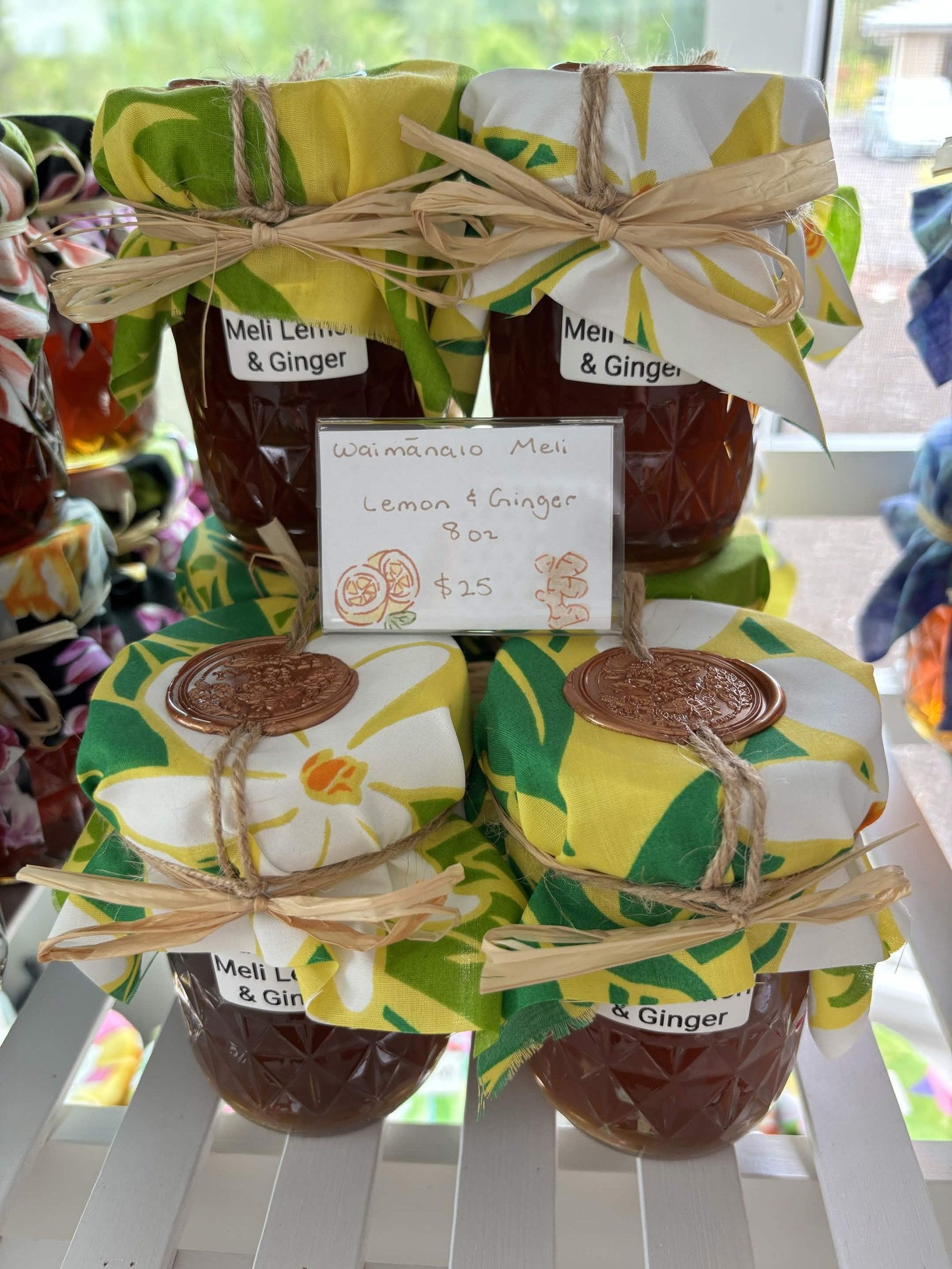 Jars of Waimānalo Meli lemon & ginger honey with yellow floral fabric lids on a white shelf