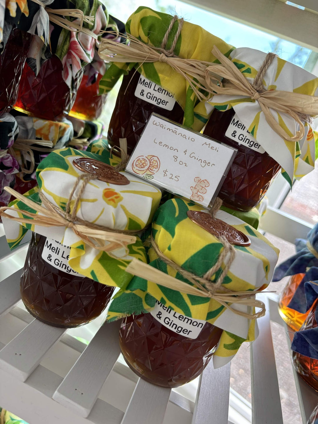 Waimānalo Meli lemon & ginger honey jars stacked beside their handwritten price card